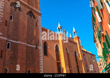 Historisches Backsteingebäude mit gotischen architektonischen Elementen in Venedig, einschließlich Spitzbögen und hohen, schmalen Fenstern. Hellblauer Himmel steht im Kontrast Stockfoto