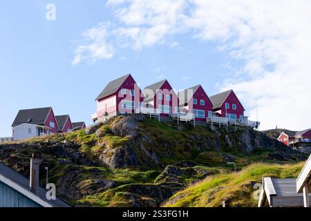 Vier rote Häuser auf einer abfallenden Felsenlandschaft mit Blick auf den historischen Teil der Stadt. sisimiut, Grönland, Dänemark, Nordamerika Stockfoto