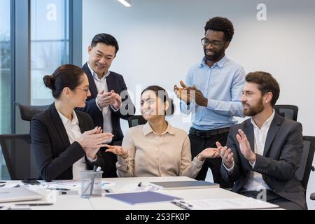 Erfolgreiches Geschäftsteam von Kollegen, die einer Frau applaudieren und gratulieren. Gruppe unterschiedlicher Personen am Arbeitsplatz, die im Büro sitzen, im Besprechungsraum. Stockfoto