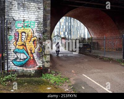 Manchester, Großbritannien, 01-04-2025: Städtisches Graffiti unter einem Backsteinbogen mit einer Person, die weggeht. Stockfoto