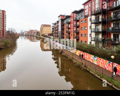 Salford , Manchester, Großbritannien, 01-04-2025: Städtischer Fluss mit farbenfrohen Graffitis und modernen Wohngebäuden. Stockfoto
