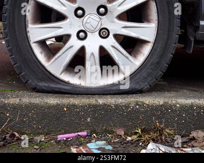 Salford, Manchester, Großbritannien, 01-04-2025: Nahaufnahme eines plattgefahrenen Autoreifens auf einer Felge in der Nähe eines Bordsteines. Stockfoto