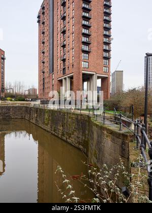Salford , Manchester, Großbritannien, 01-04-2025: Hohes Wohnhaus aus Backstein, das sich in einer ruhigen städtischen Wasserstraße spiegelt. Stockfoto