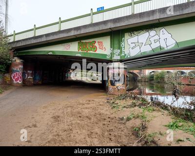 Salford , Manchester, Großbritannien, 01-04-2025: Graffiti-bedeckte Brücke über einen ruhigen Kanalweg an einem bewölkten Tag. Stockfoto