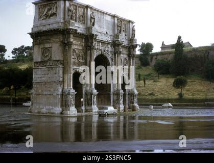 1970, ein Auto aus der Zeit, parkt am Konstantinsbogen, einem Triple Bogendenkmal in Rom, Italien. Das 1315 errichtete Denkmal zum Gedenken an den Sieg von Kaiser Konstantin über Maxentius befindet sich zwischen dem Kolosseum und dem Palatin, an der Via Triumphalis, einer breiten Straße, die später zu Fußgängerzonen geführt wurde. Stockfoto