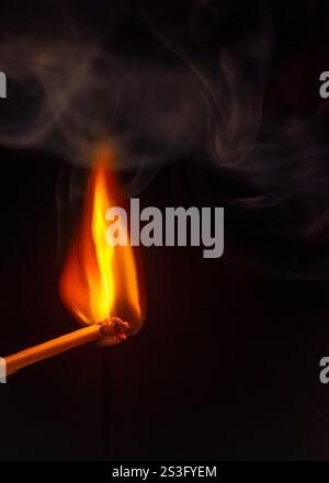 Brennender Streichholzstab mit etwas Rauch auf schwarzem Hintergrund Stockfoto