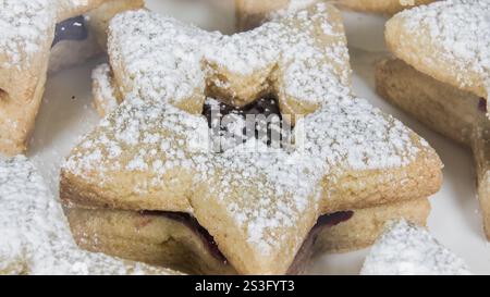 Festliche, sternförmige Kekse gefüllt mit Marmelade und mit Puderzucker überzogen schaffen ein süßes Urlaubsvergnügen, perfekt zum Teilen. Stockfoto