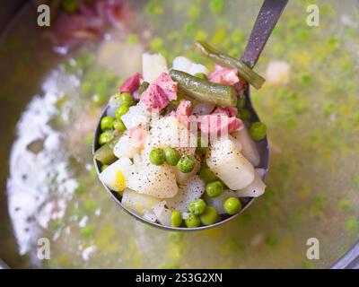 Eine Kelle voll Schinken, Kartoffeln und Erbsensuppe aus dem Topf holen. Stockfoto