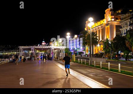 Nächtlicher Blick auf Jogger und Fußgänger, die einen milden Abend auf der historischen Promenade des Anglais am Meer in der Cote d'Azur genießen Stockfoto