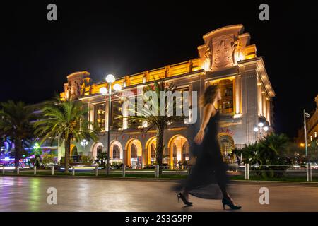 Eine Frau in einem schwarzen Kleid ist bewegungsunscharf, während sie entlang der beleuchteten Promenade des Anglais an der französischen Riviera in Nizza, Frankreich, spaziert Stockfoto