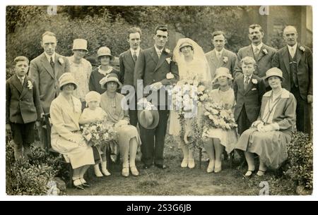 Die Frauen tragen modische Cloche-Hüte, Brautbekleidung, Braut und Bräutigam und Brautjungfern, historische Kostüme, junge und ältere Leute, die für ein Hochzeitsfoto im Freien posieren, wunderschöne Sträuße und Posen, Blumen 1920. GROSSBRITANNIEN Stockfoto