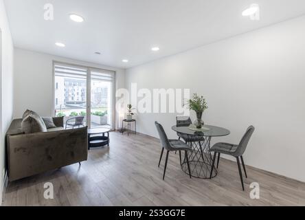 Modernes Wohnzimmer mit offenem Bereich, Sofa und Esstisch. Blumen auf dem Tisch. Fenster im Hintergrund. Hartholzboden. Breit Stockfoto