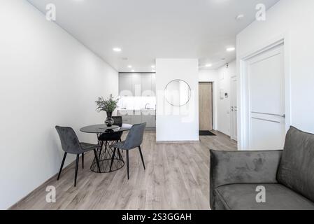 Modernes Wohnzimmer mit offenem Bereich, Sofa und Esstisch. Blumen auf dem Tisch. Küchenbereich im Hintergrund. Hartholzboden. Stockfoto