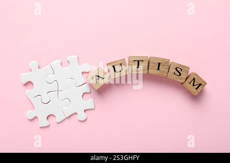 Wort Autismus gemacht mit Holzwürfeln und Puzzleteilen auf rosa Hintergrund, flach gelegt Stockfoto