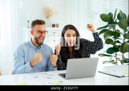 Motiviertes, glückliches Business-Team feiert Erfolg am Schreibtisch, multirassische Kollegen analysieren Diagramme und erreichen Ziele mit einem Notebook, das Ergebnisse anzeigt, Teamarbeit in einem modernen Büro Stockfoto