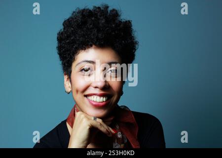 Freundliche braune Frau, die lächelt und in die Kamera blickt. Weibliches Modell mit kurzen lockigen Haaren. Die afro-amerikanische Dame trägt ein schwarzes Hemd und einen braunen Schal. Stockfoto