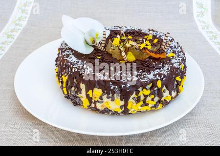 Ein wunderschön gefertigter Schokoladenkuchen sitzt elegant auf einem weißen Teller, der mit leuchtenden gelben Streuseln und zarten essbaren Blumen geschmückt ist Stockfoto