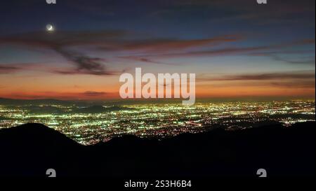 Wunderschöner orangefarbener Sonnenuntergang mit Mond über den Lichtern der Stadt San Bernardino Stockfoto