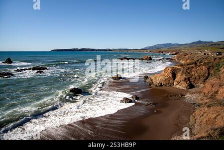 Eine ruhige Küstenlinie in Cambria, Kalifornien, erstreckt sich entlang der Küste, wo Wellen sanft auf Felsen am Pacific Coastal Highway prallen Stockfoto