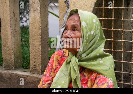 Eine traurig aussehende ältere Minangkabau-Frau, die einen grünen Hijab und ein Blumenkleid vor einer gelben Wand in Bukittinggi, West Sumatra, Indonesien trägt. Stockfoto