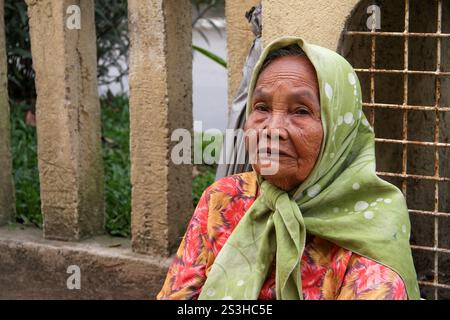 Eine traurig aussehende ältere Minangkabau-Frau, die einen grünen Hijab und ein Blumenkleid vor einer gelben Wand in Bukittinggi, West Sumatra, Indonesien trägt. Stockfoto