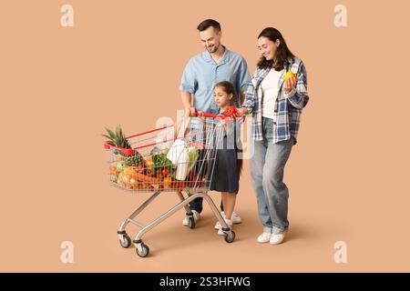 Glückliche Familie mit vollem Einkaufswagen und Paprika auf beigefarbenem Hintergrund Stockfoto