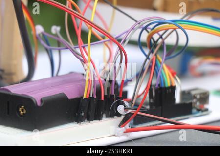 Satz von Überbrückungskabeln, die mit Mikrocontroller und Steckplatine verbunden sind, mit einer Batterie als Teil der Prototypenerstellung für Elektronikprojekte Stockfoto