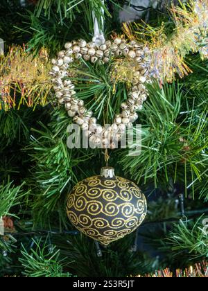 Ein Weihnachtsbaum mit herzförmiger Dekoration und einem schwarz-goldenen Glitzerschmuck und goldenem Lametta hängen davon Stockfoto