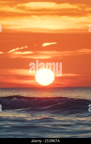 Nahaufnahme der Wellen am Strand und eines wunderschönen Sonnenaufgangs über dem Meer, vertikales Foto Stockfoto