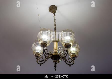Ein wunderschön gefertigter Kronleuchter mit sechs Glaslaternen hängt von der Decke und strahlt ein warmes Licht über den elegant eingerichteten Raum, Showcas Stockfoto