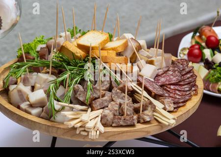 Eine lebendige Platte gefüllt mit verschiedenen Wurstwaren, Käse und frischen Kräutern wird bei einem geselligen Treffen präsentiert. Diese Umgebung im Freien sorgt für eine perfekte Atmosphäre Stockfoto