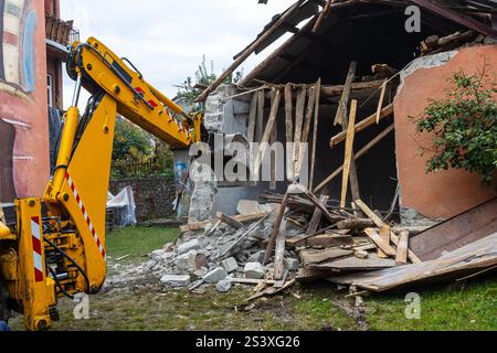 Ein Bagger zerstört aktiv ein altes Gebäude innerhalb eines Wohnviertels und streut Schutt wie Holz und Beton um den Standort. Die Stockfoto