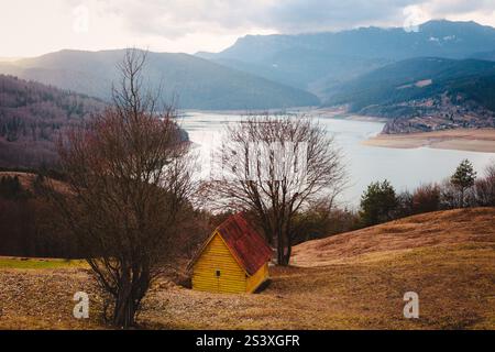 Einsames Holzhaus in den Bergen mit Blick auf den See. Das Haus liegt zwischen den Bäumen. Herbstlandschaft. Stockfoto