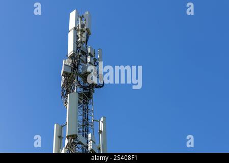 Weiße Antennen mit Kabeln am Mobilfunkturm in Nahaufnahme. Mobiler Datenübertragungsturm mit Antennen vor blauem, klarem Himmel, Konzept der Telekommunikation Stockfoto