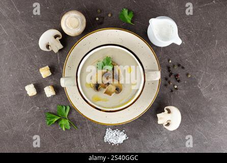Pilzcremesuppe mit Zutaten zum Kochen: Champignons, Croutons, Sahne, Gewürze und Petersilie. Brauner Hintergrund. Stockfoto