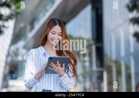 Die Frau hält eine Tafel und lächelt. Sie trägt ein gestreiftes Hemd. Die Tablette liegt in ihrer Hand Stockfoto