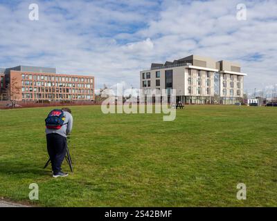 Blick über einen grünen Raum zum Senate House, Waterside Campus, University of Northampton, UK; Fotostudentin macht Fotos im Vordergrund Stockfoto