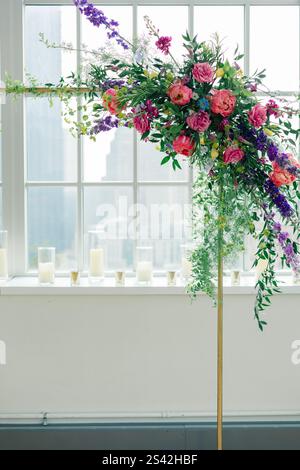 Blumenbogen mit rosa und lila Blumen an einem hellen Fenster. Stockfoto