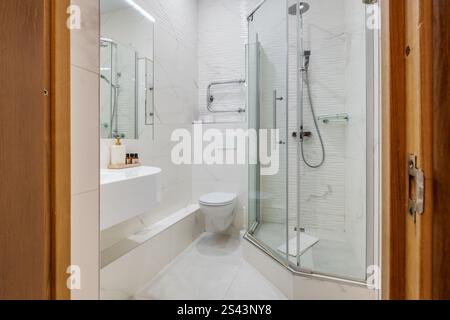Ein sauberes und modernes Bad mit Glasdusche, wandmontierter Toilette, Handtuchwärmer und Fliesen im Marmorstil. Stockfoto