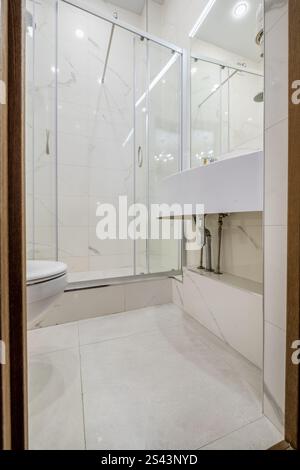 Ein sauberes und modernes Bad mit Glasdusche, wandmontierter Toilette, Handtuchwärmer und Fliesen im Marmorstil. Stockfoto