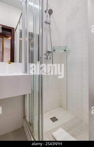 Ein sauberes und modernes Bad mit Glasdusche, wandmontierter Toilette, Handtuchwärmer und Fliesen im Marmorstil. Stockfoto