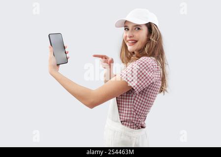 Glückliche Frau in Maleranzüge, die Telefon für Online-Shopping von Farben und Produkten zeigt, um Hauswände zu malen und das Haus zu renovieren, isoliert auf Stockfoto