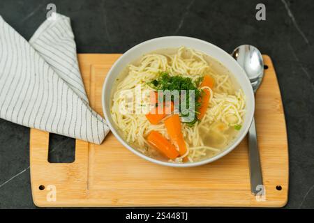 Aus nächster Nähe sehen Sie eine Schüssel mit hausgemachter Hühnchennudelsuppe, garniert mit frischem Dill und lebhaften Karottenscheiben. Das Gericht ist Stockfoto