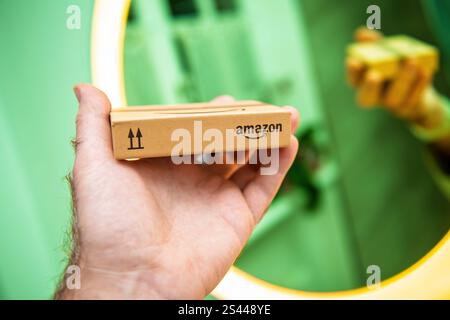 Paris, Frankreich – 22. November 2021: Nahaufnahme eines kleinen Amazon-Pakets, das in einer Hand vor einem leuchtend grünen Hintergrund gehalten wird und minimalistisches Branding zeigt Stockfoto