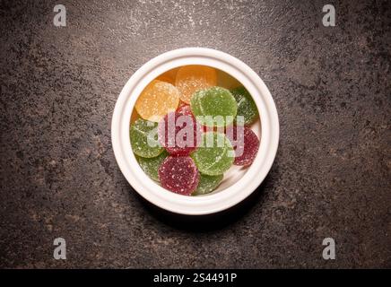 Untertasse mit bunten Marmeladenkugeln auf schwarzem Küchentisch, Draufsicht, Nahaufnahme Stockfoto