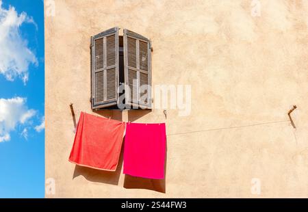 Gelbe Hauswand mit Holzfenster. Bunte Handtücher, die an sonnigen Tagen aufgehängt werden, werden getrocknet Stockfoto