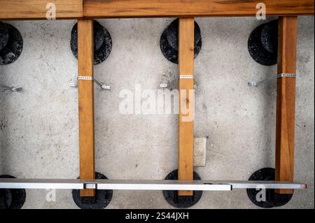 Nahaufnahme von Holzträgern, die an schwarzen verstellbaren Stützen befestigt sind, die mit Metallbändern auf einem Betonsockel befestigt sind und die Konstruktionsdetails zeigen. Stockfoto