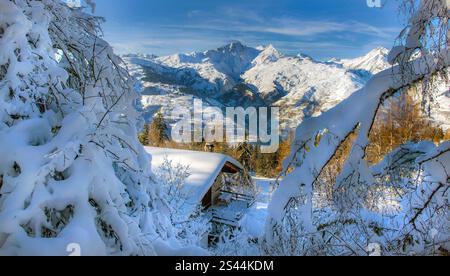 Winterlandschaft in alpinem französischem Berg bedeckt mit Schnee unter blauem Himmel und schneebedecktem Chalet zwischen schneebedeckten Baumzweigen Stockfoto