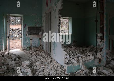 Das Innere eines mit Bauschutt gefüllten, verrotteten Raumes mit einer kaputten Wand, abblätternder Farbe und einer offenen Tür, die zu einer Steinmauer führt Stockfoto