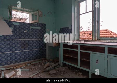Verfallene Küche mit kaputten Fenstern und abblätternder Farbe in einem verlassenen Haus, die den städtischen Verfall veranschaulicht Stockfoto